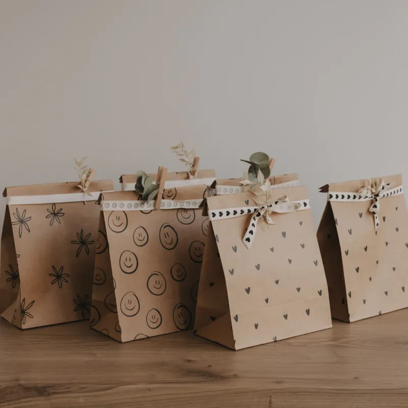 Papier Geschenktüten mit Herz-, Smiley- und Blumenmotiven im Set, dekorativ aufgereiht auf Holztisch